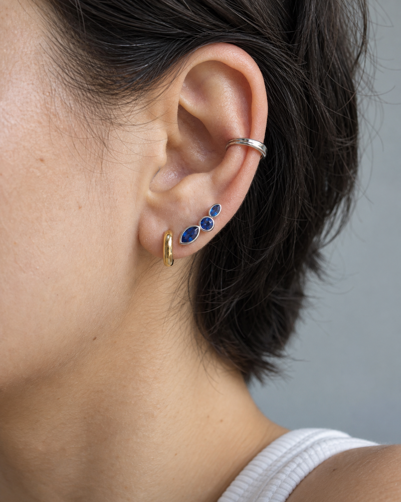 AI design reference: a model wearing a blue sapphire ear climber with a cuff and small hoop.